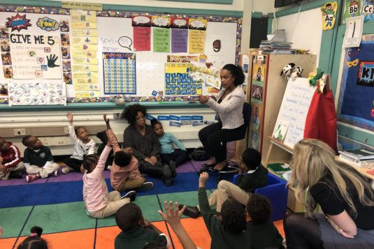 young students raise habds and a classroom teacher calls on them