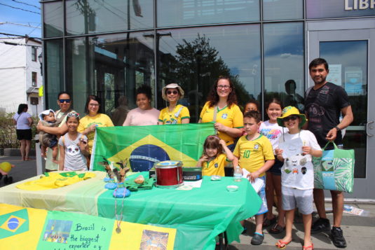 A group of parents and children stand behind a table with Brazilian flags and items